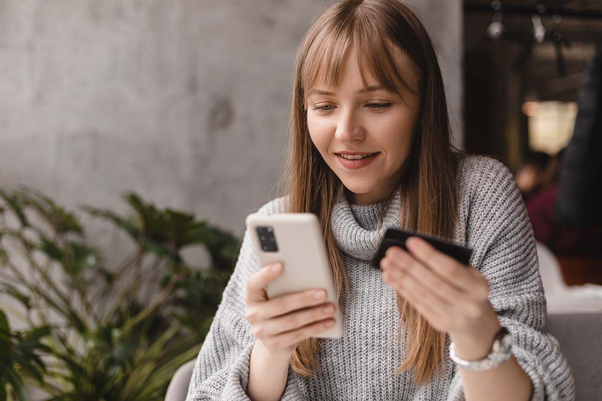 Woman holding her phone, shopping while also holding her credit card